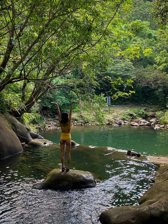 Gi Shieh wearing a yellow high-waist bikini standing on the second tier of Huiyao Waterfall in Taipei with arms extended
